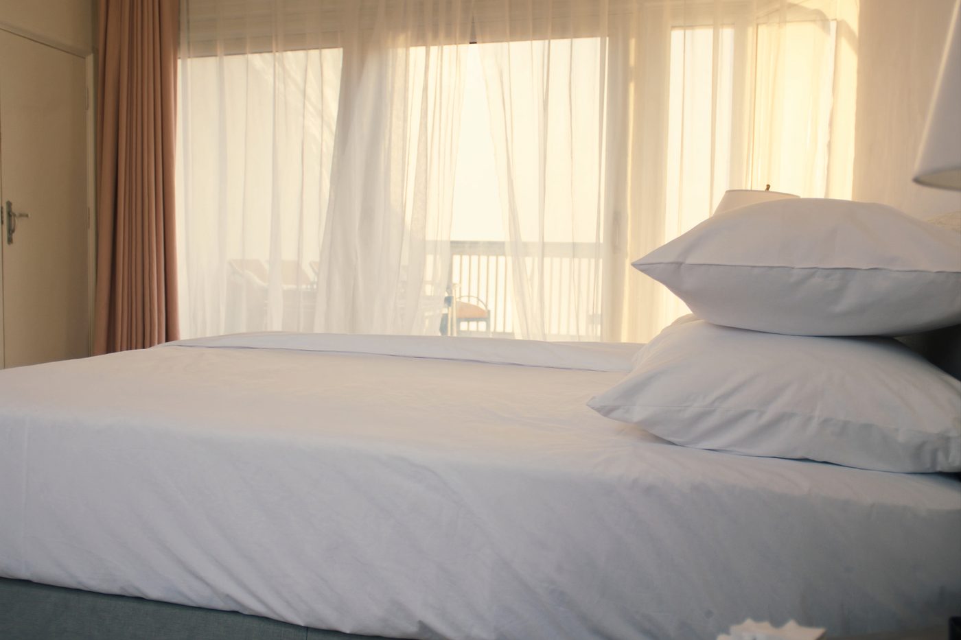 Bright Mediterranean villa bedroom with crisp white linens and sunlit curtains